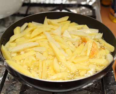 Картофель порезанный соломкой жарится на сковороде