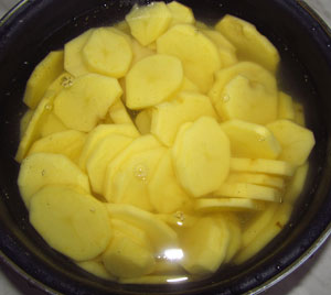 Картофель нарезанный тонкими ломтиками помещен в холодную воду