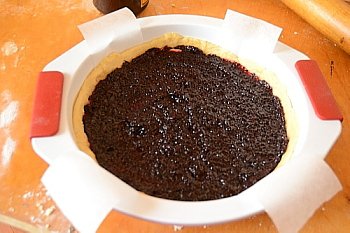 В форму помещено тесто и сверху выложен слой варенья из черной смородины