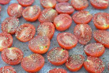 Помытые помидоры разрезанные пополам на пергаменте и посыпанные солью и травами