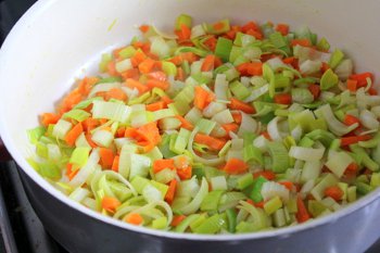 Порезанные морковь сельдерей и лук порей в сковороде