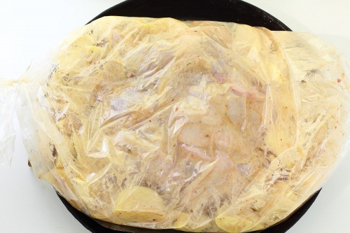 Нарезанный картофель с луком, специями и чесноком в миске в рукаве для запекания - целая курица с картошкой в рукаве